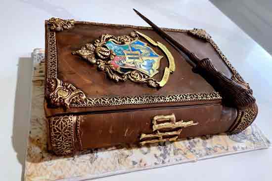 Torta in pasta di zucchero a tema Harry Potter a forma di libro con stemma di Hogwarts e bacchetta