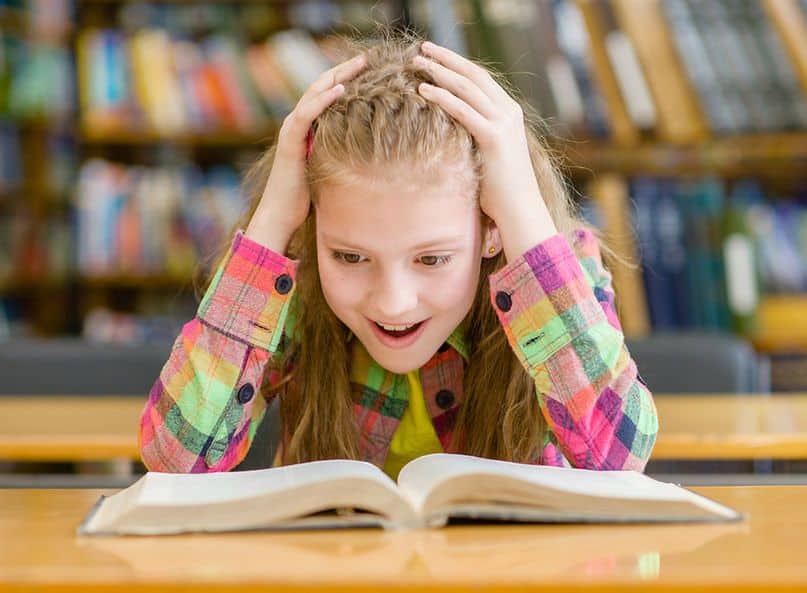Foto bambina di 11 anni che legge un libro in biblioteca